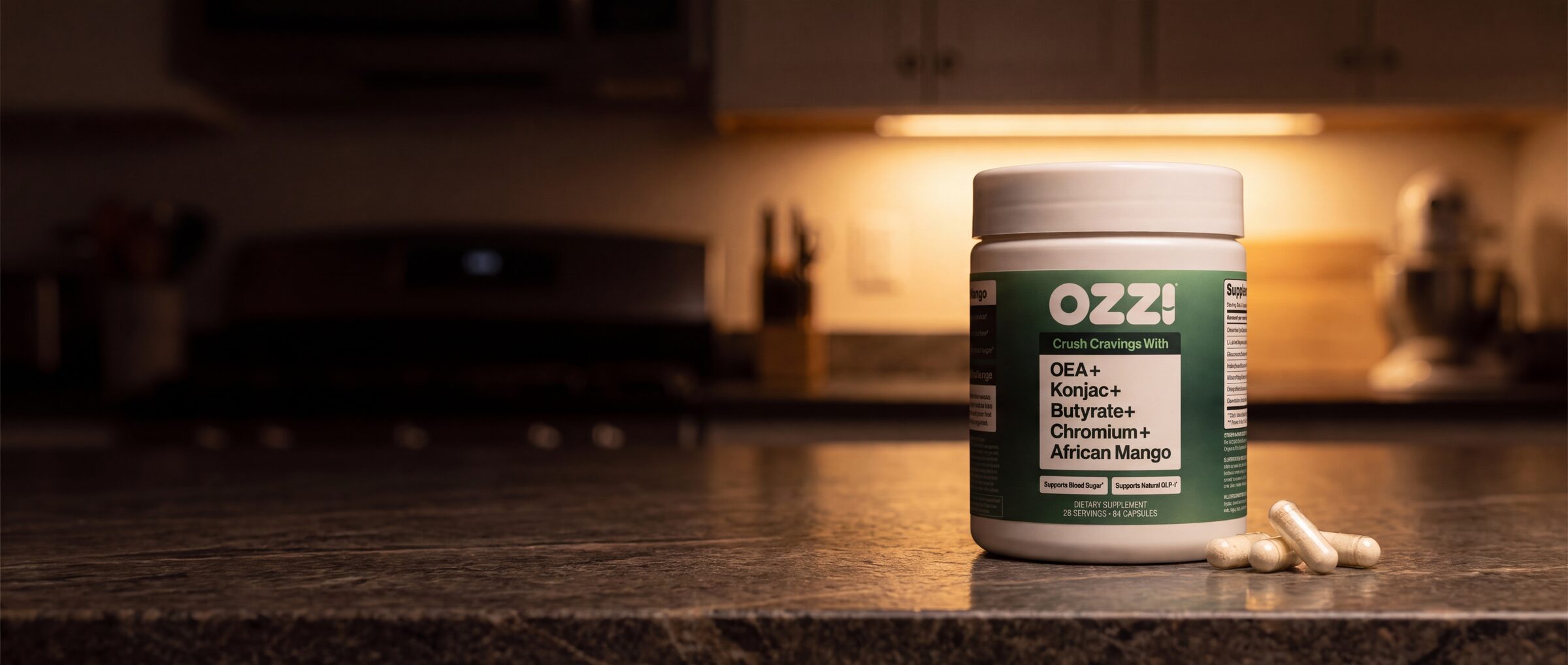 Ozzi capsule bottle and capsules on a kitchen counter at night under a warm cabinet light