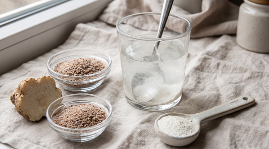A glass of fiber powder dissolving in water beside psyllium husk and konjac root on a linen surface