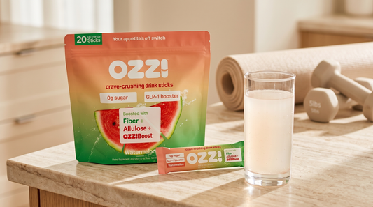 OZZ! watermelon pouch, a single stick pack, and a glass of the prepared Ozzi drink on a kitchen counter beside a yoga mat and dumbbells