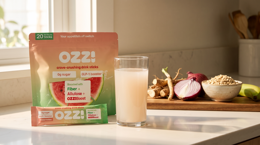 An Ozzi Crave Crusher pouch, a single stick pack, and a glass of the prepared drink on a sunlit kitchen counter beside chicory root, red onion and oats