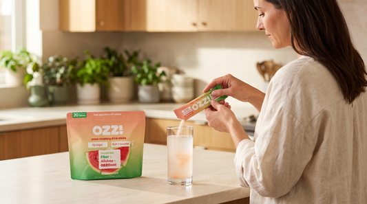 A woman pouring an Ozzi watermelon stick pack into a glass of cold water on a bright kitchen counter