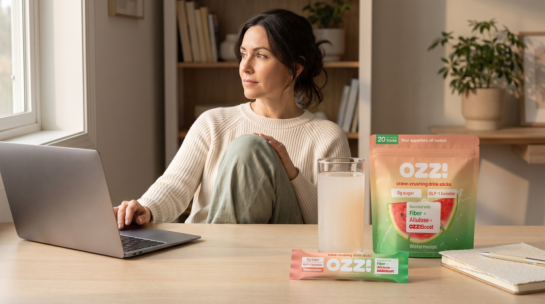 Woman at a home office desk with an Ozzi watermelon pouch, a stick pack, and a glass of the prepared drink