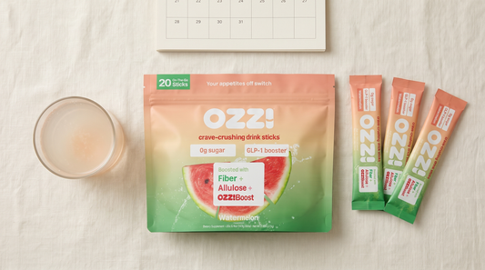 Overhead flatlay of the Ozzi watermelon pouch, three drink sticks, a glass of the prepared drink and a calendar page on cream linen