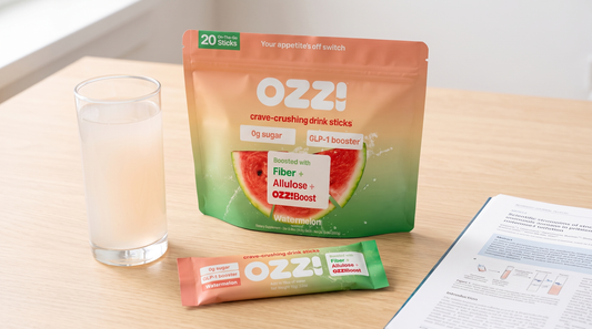 Ozzi watermelon pouch and stick pack on a light wood desk beside a glass of the prepared drink and a printed scientific paper