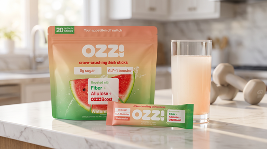 Ozzi watermelon drink stick pouch, a single stick and a glass of the prepared drink on a marble kitchen counter with dumbbells in the background