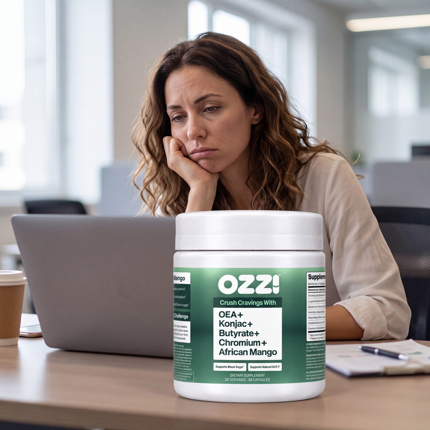A woman at her desk mid-afternoon, chin in hand, with a bottle of Ozzi capsules in front of her