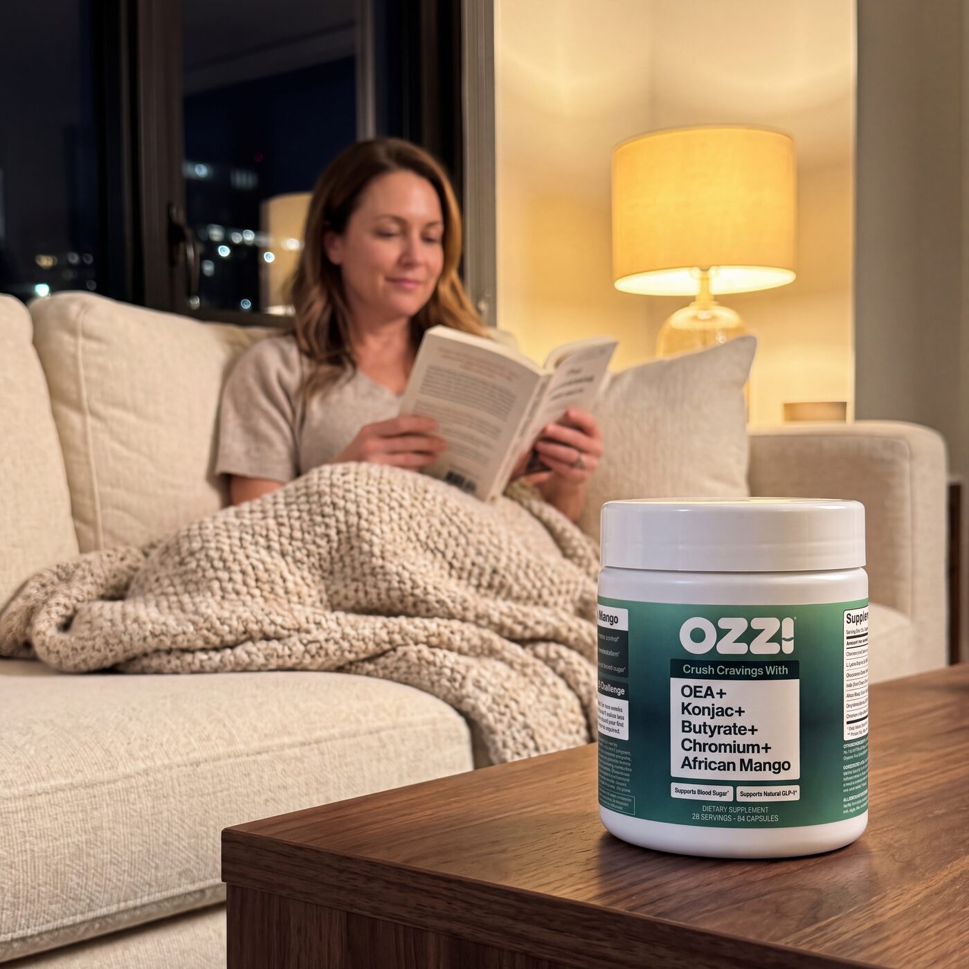 A woman relaxes on the couch with a book, a bottle of Ozzi capsules on the table
